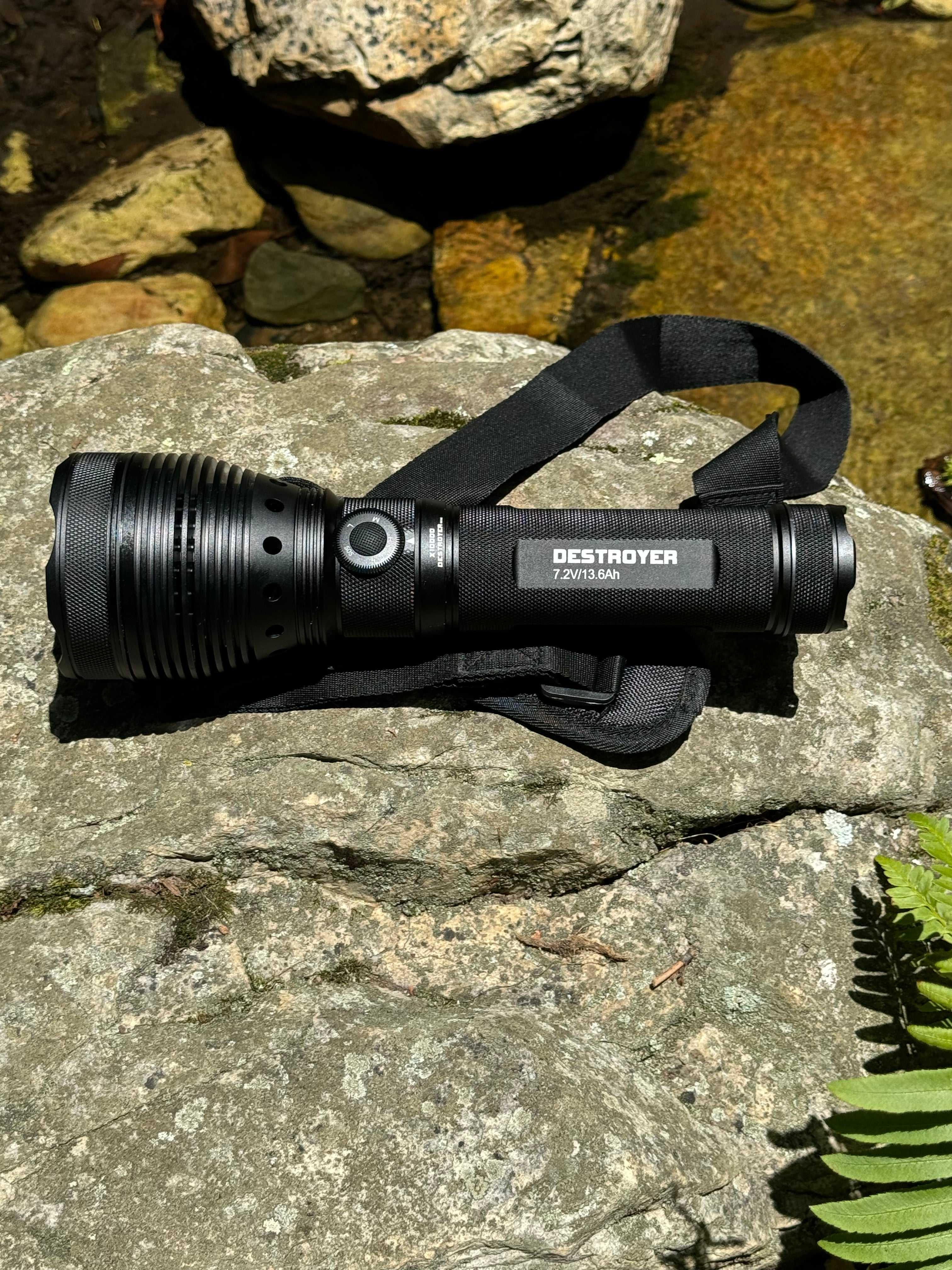 Black flashlight with a strap on a rock by a water source